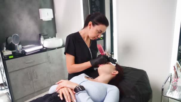 Master makes permanent eyebrow makeup procedure to woman in beauty salon. - Footage, Video