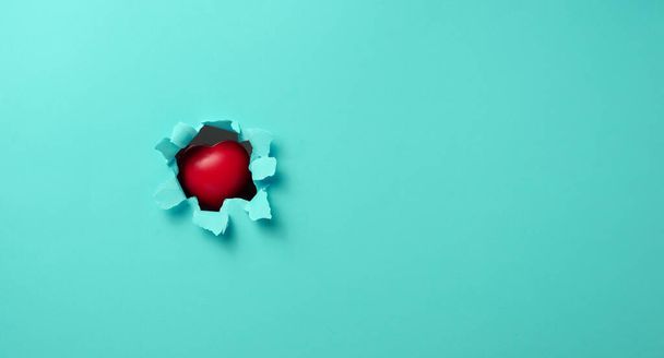 red heart sticks out in a hole with torn edges in blue paper, copy space - Foto, immagini