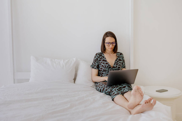 a European woman in a gray linen robe is working on a laptop at home or resting. a millennial woman is watching a movie on a laptop and having fun - Fotografie, Obrázek