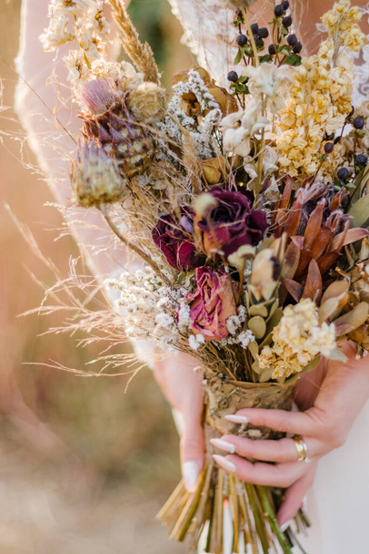 A closeup of a bride holding a wedding bouquet made of dried flowers - Foto, afbeelding