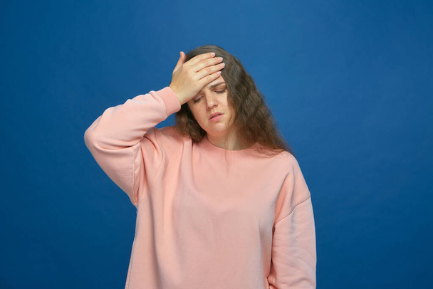 Exhausted ill young girl suffer headache touching forehead, closed eyes from strong migraine pain on blue background - Фото, изображение