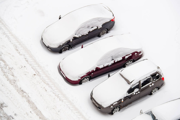 Auta na parkovišti pokrytá sněhem. Automobily sněží unášené u silnice na dvoře domu. Letecký pohled shora. Koncept špatného zimního rána. - Fotografie, Obrázek