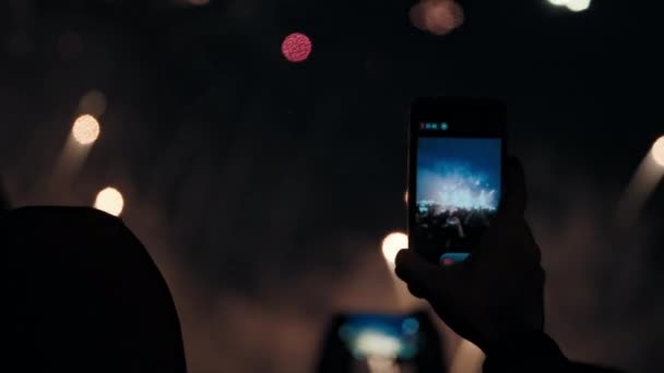 Handen vasthouden smartphones en schieten video 's van exploderend vuurwerk in de nachtelijke hemel. - Video