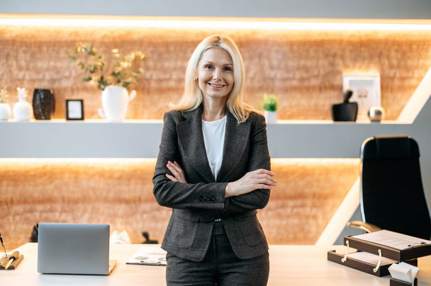 Portrait successful beautiful happy smart caucasian mature blonde business woman, top manager, recruitment specialist, stand in modern office in formal suit, looking at camera, arms crossed, smiling - Photo, Image