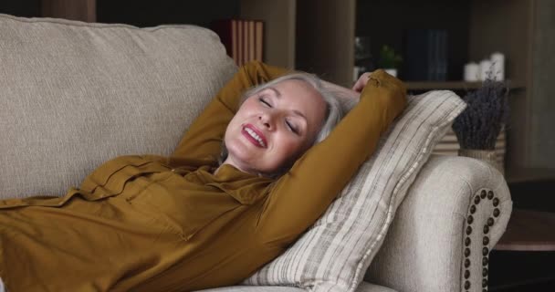 Serene elderly woman lying on sofa resting breathing fresh air - Кадры, видео