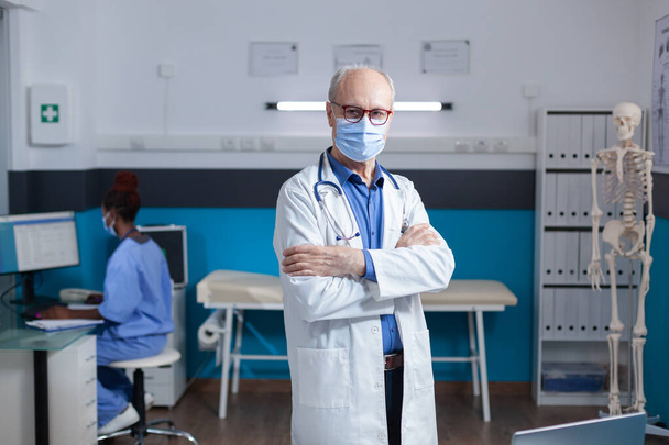 Retrato de homem médico vestindo máscara facial e casaco branco, de pé com os braços cruzados - Foto, Imagem