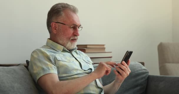 Ancianos uso masculino teléfono inteligente se siente sorprendido emocionado celebrar premio ganador - Metraje, vídeo