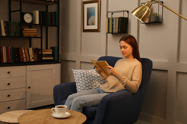 Young woman reading book in armchair indoors. Home library - Foto, immagini
