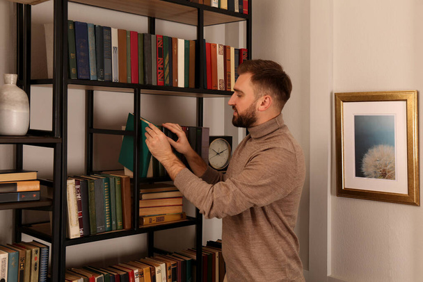 Young man choosing book on shelf in home library - Фото, зображення