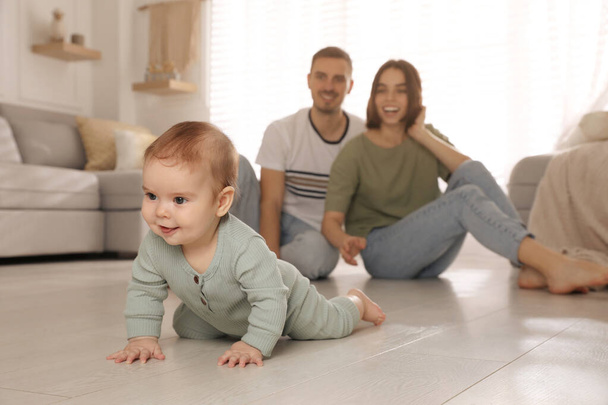 Happy parents watching their cute baby crawl on floor at home - Fotó, kép