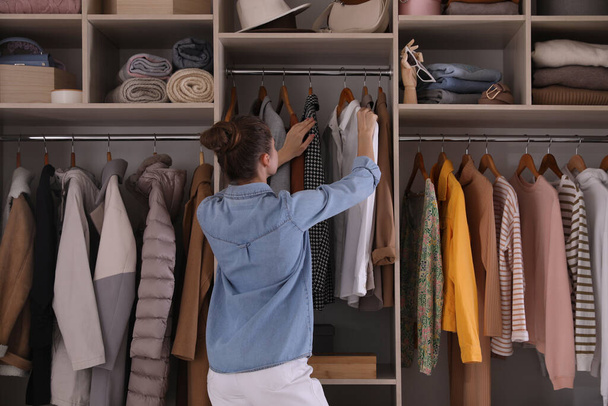 Mujer joven eligiendo ropa en armario armario, vista trasera - Foto, Imagen