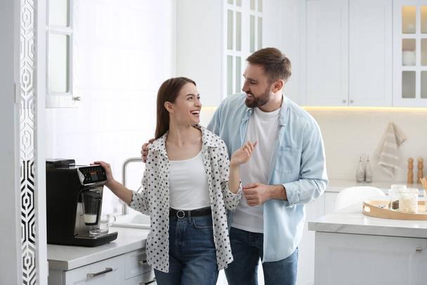 Happy couple preparing fresh aromatic coffee with modern machine in kitchen - Zdjęcie, obraz