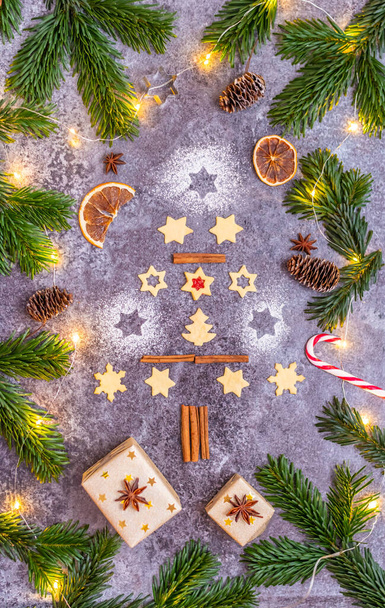 Christmas sweets and cookies in form of christmas tree placed on gray desk with pine cone and branch on the side. Winter and christmas decorations, small glowing light on the side - Foto, Imagem