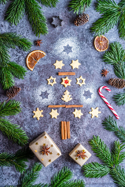 Christmas sweets and cookies in form of christmas tree placed on gray desk with pine cone and branch on the side. Winter and christmas decorations, cinnamon, sugar and star anise. - Foto, afbeelding