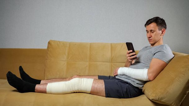 膝を負傷し腕を骨折した男が電話でスクロール - 写真・画像