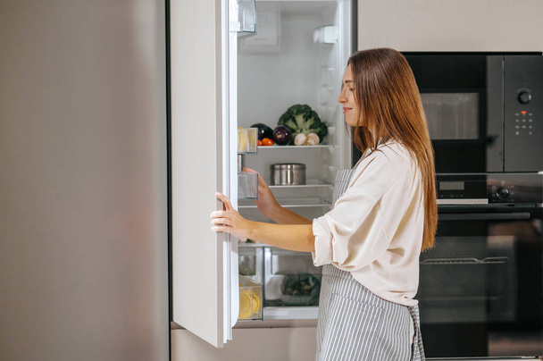 fiatal nő, figyelembe véve az élelmiszer-tól a hűtő - Fotó, kép