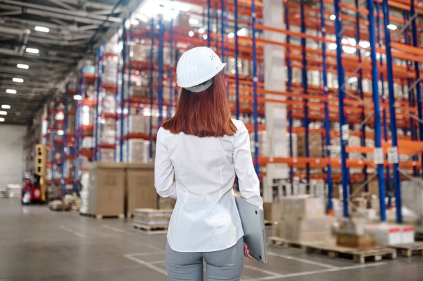 Woman with laptop in warehouse with back to camera - Foto, imagen