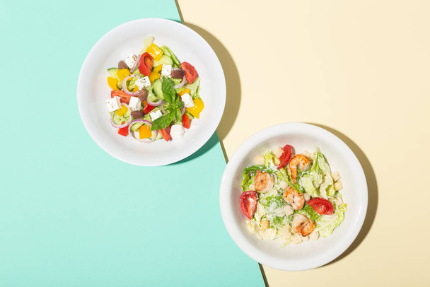 Greek salad and Cesar salad in white plates hard shadows on blue and yellow - 写真・画像