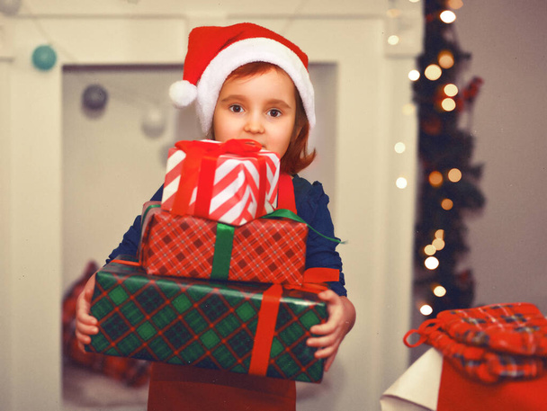 Child little cute girl kid in Santa cap holding a Christmas gift boxes in a hands. - Fotoğraf, Görsel