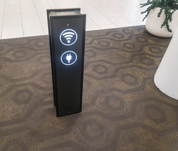 Detailní záběr telefonního nabíjecího stánku přes USB a Wi-Fi zónu na letišti nebo v supermarketu, nedaleké rostliny v bílých květináčích. - Fotografie, Obrázek