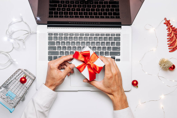 Kerstmis online winkelen. Geschenkdoos rood lint, trolley en laptop, dollar in platte lay internet shopping compositie. Kerstwinkel, bovenaanzicht - Foto, afbeelding