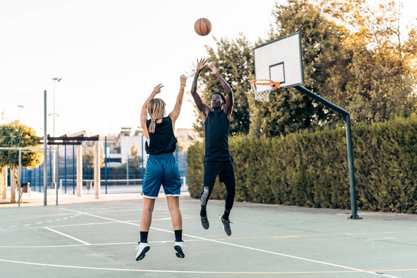 Blonde woman shooting a ball at the basket while a man defends it - Foto, Bild