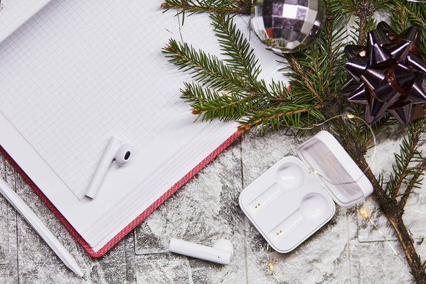 Wireless earphones on notepad mock up with Christmas decorations. Freelance, remote work, taking webinar, calling to family concept. New years goals and resolutions mock up.  - Фото, изображение