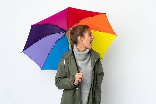 Mladá žena drží deštník izolované na bílém pozadí se smíchem v boční poloze - Fotografie, Obrázek