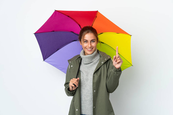Young woman holding an umbrella isolated on white background showing and lifting a finger in sign of the best - Фото, зображення