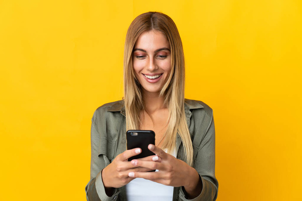 Jonge blonde vrouw geïsoleerd op gele achtergrond verzenden van een bericht of e-mail met de mobiele - Foto, afbeelding
