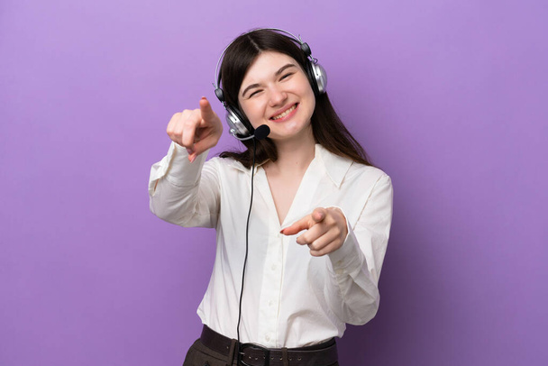 Telemarketer Russian woman working with a headset isolated on purple background points finger at you while smiling - Photo, Image