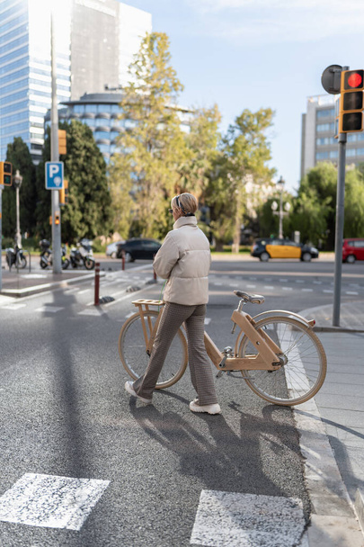 Женщина с велосипедом пересекает асфальтированную дорогу - Фото, изображение