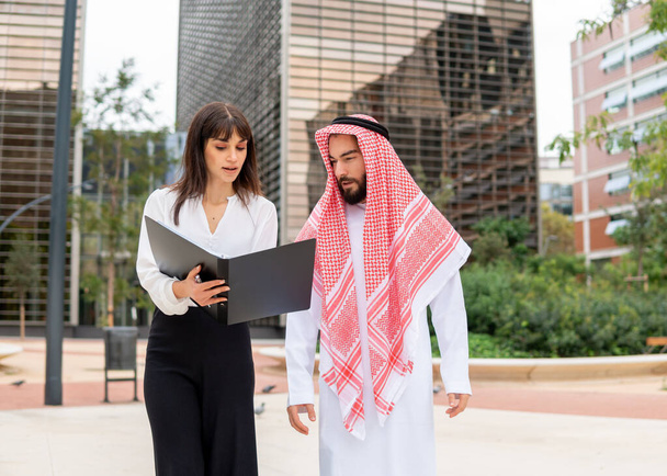 Junge europäische Geschäftsfrau erklärt arabischem Mann bei Outdoor-Treffen Vertragsdetails - Foto, Bild