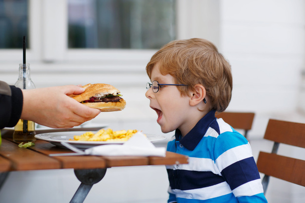 kleine jongen eten fastfood: Franse frietjes en hamburger - Foto, afbeelding