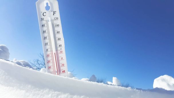 The thermometer lies on the snow and shows a negative temperature in cold weather on the blue sky.Meteorological conditions with low air and ambient temperatures.Climate change and global warming - Photo, image