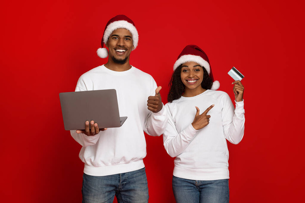 Gelukkig paar in Santa hoeden met laptop en creditcard - Foto, afbeelding