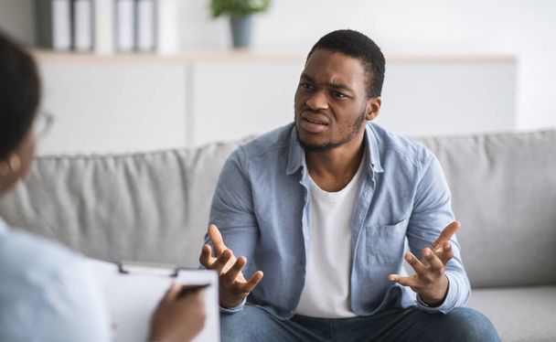 Psychologist helping depressed young black man, giving consultation to male patient at office - Foto, afbeelding