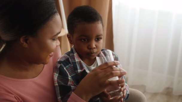 Caring Black Mother Giving Her Preschooler Son Glass Of Water At Home - Filmati, video