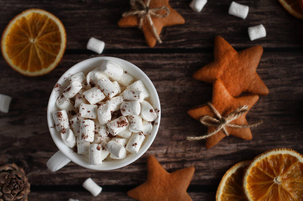 mug with marshmallows, ginger cookies with stars, orange slices, cones on a wooden background - Fotografie, Obrázek