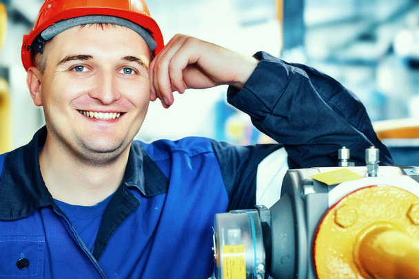 To portret pracownika w kasku i ubraniu. Uśmiechnięty inżynier kaukaskiego wyglądu w fabryce lub zakładzie przemysłowym. - Zdjęcie, obraz