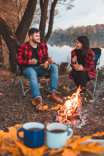 smiling happy couple resting near fire cooking food autumn camping concept - Photo, Image