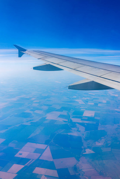 View from the airplane window at a beautiful clear blue sky and the airplane wing. Earth and sky as seen through window of an airplane. - Foto, Imagen