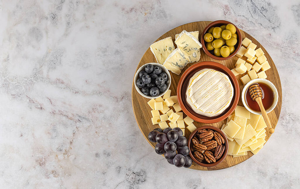 Bovenaanzicht van smakelijke Charcuterie bord met kaas, druif, noten, olijven, en ham op een cirkel keukenplaat op de achtergrond van marmeren steen, bovenaanzicht, kopieerruimte. Gastronomisch eten, kopieerruimte. - Foto, afbeelding