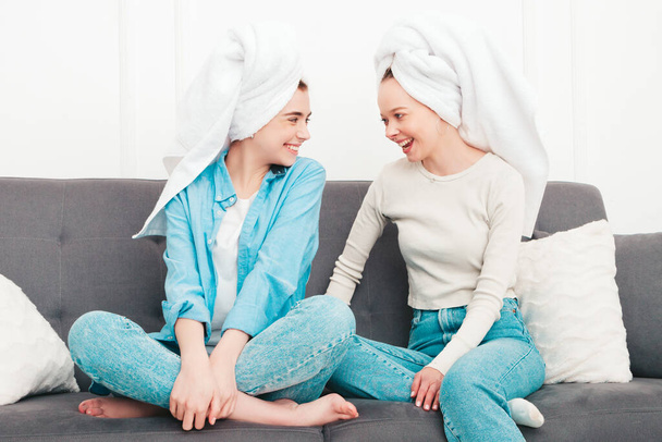 Two young beautiful smiling women sitting at the sofa. Sexy carefree models posing indoors in posh apartment or hotel room. They doing beauty treatments at home in towels on heads - Fotoğraf, Görsel