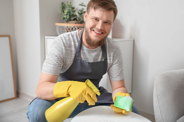 Young man with sponge cleaning table at home - Foto, afbeelding