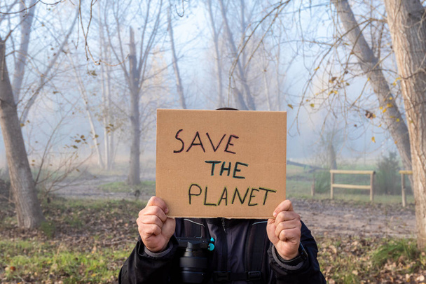 The Male hands hold a cardboard sign with the slogan Save the Planet with the forest in background - Φωτογραφία, εικόνα