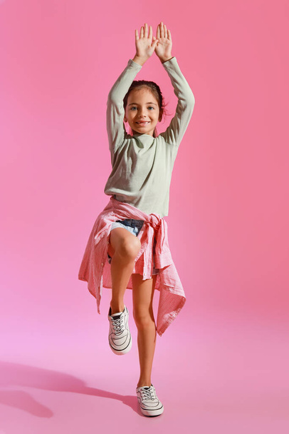 Красивая маленькая девочка танцует на розовом фоне - Фото, изображение