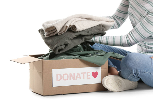 Junge Frau steckt Spendenkleidung in Schachtel auf weißem Hintergrund - Foto, Bild