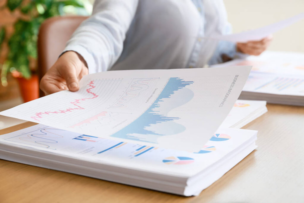 Businesswoman taking paper sheet with diagrams at desk in office, closeup - Fotó, kép