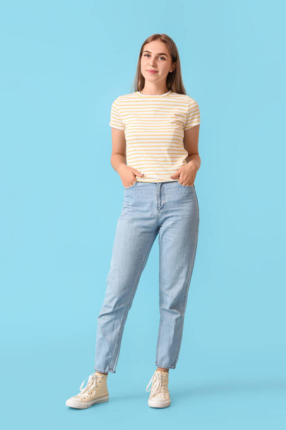 Hezká mladá žena na sobě pruhované tričko a džíny na modrém pozadí - Fotografie, Obrázek
